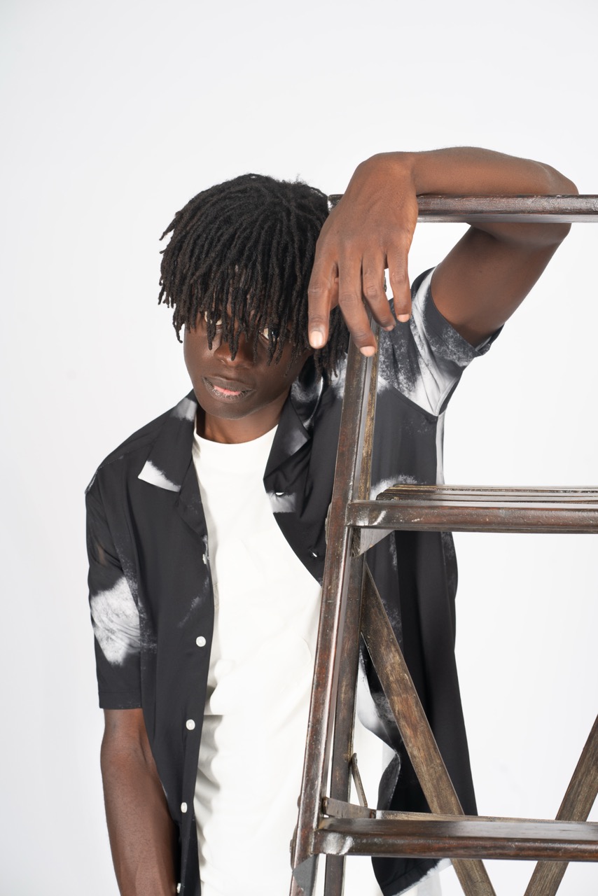 Young black man with locs leaning on a wooden ladder against a white backdrop. Photoshoot at Mild Studios Toronto, Ontario. Nissi Pululu Photographer 