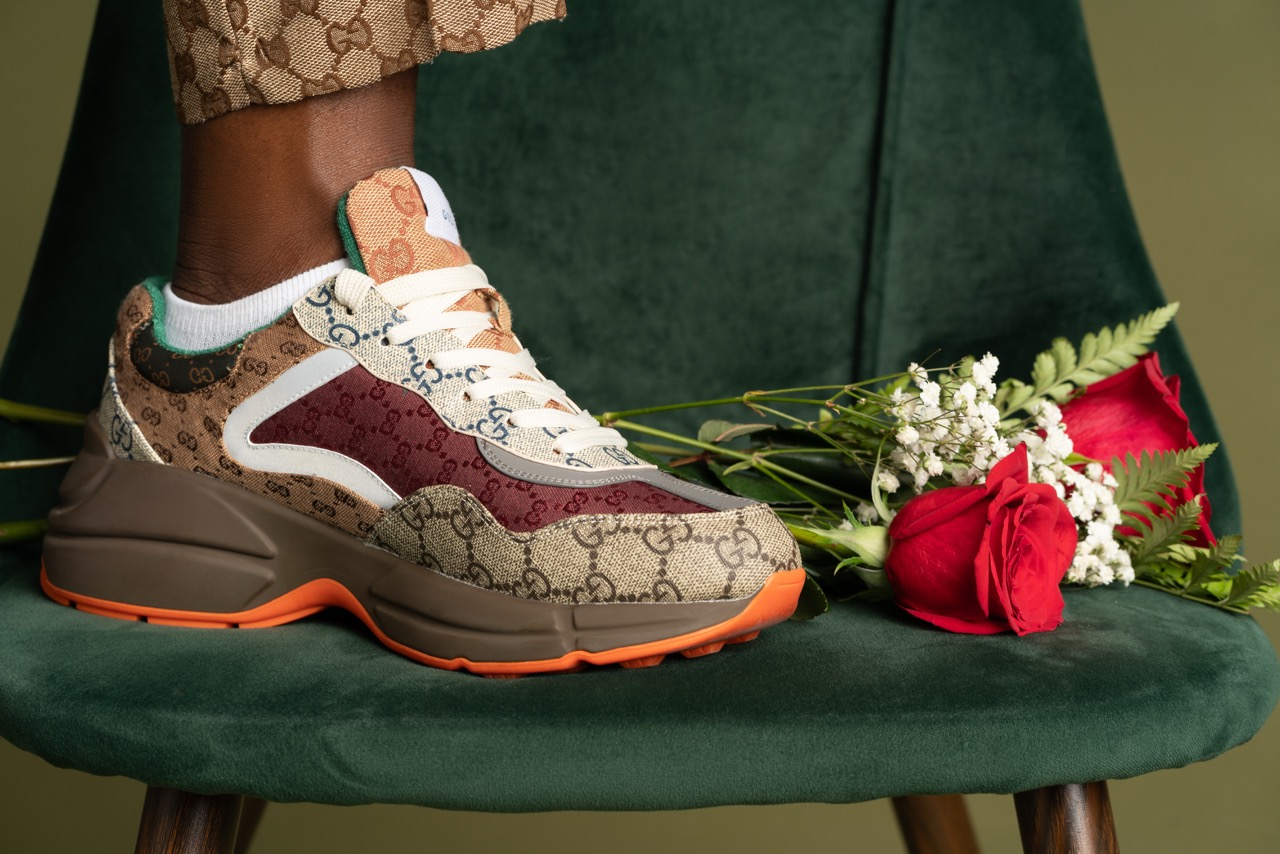 Close up of a patterned sneaker resting on a green velvet chair beside red roses. Picture Day, a shoot by Nissi Pululu of Sonset Inc in Toronto