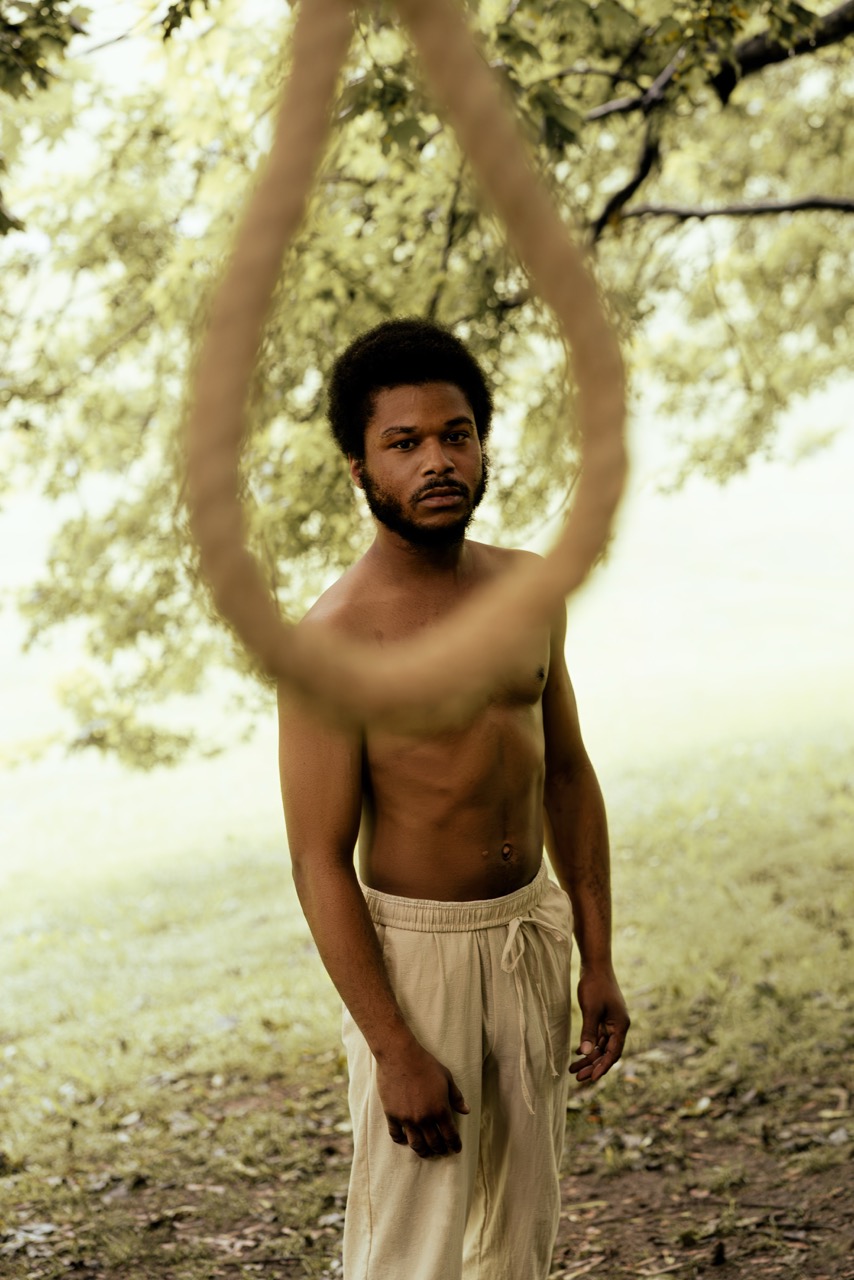Man standing outdoors behind a large hanging rope loop with trees behind him. Freedom, a shoot by Nissi Pululu of Sonset Inc in Toronto